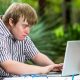 Jovem sentado com Síndrome de Down digitando num laptop. Mostrando a capacidade de superação e vontade de socializar-se.