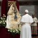 Linda imagem de Maria, de manto branco com flores brancas em volta da image, Papa Francisco de pé reza em silêncio.